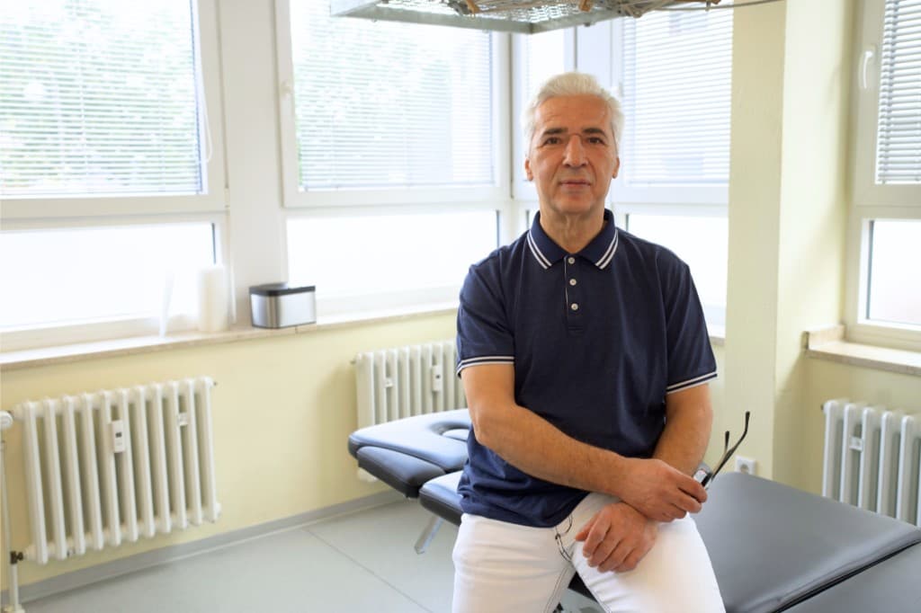 Physiotherapeut führt eine manuelle Mobilisation am Arm eines Patienten in einer hellen Behandlungsraum-Praxis.